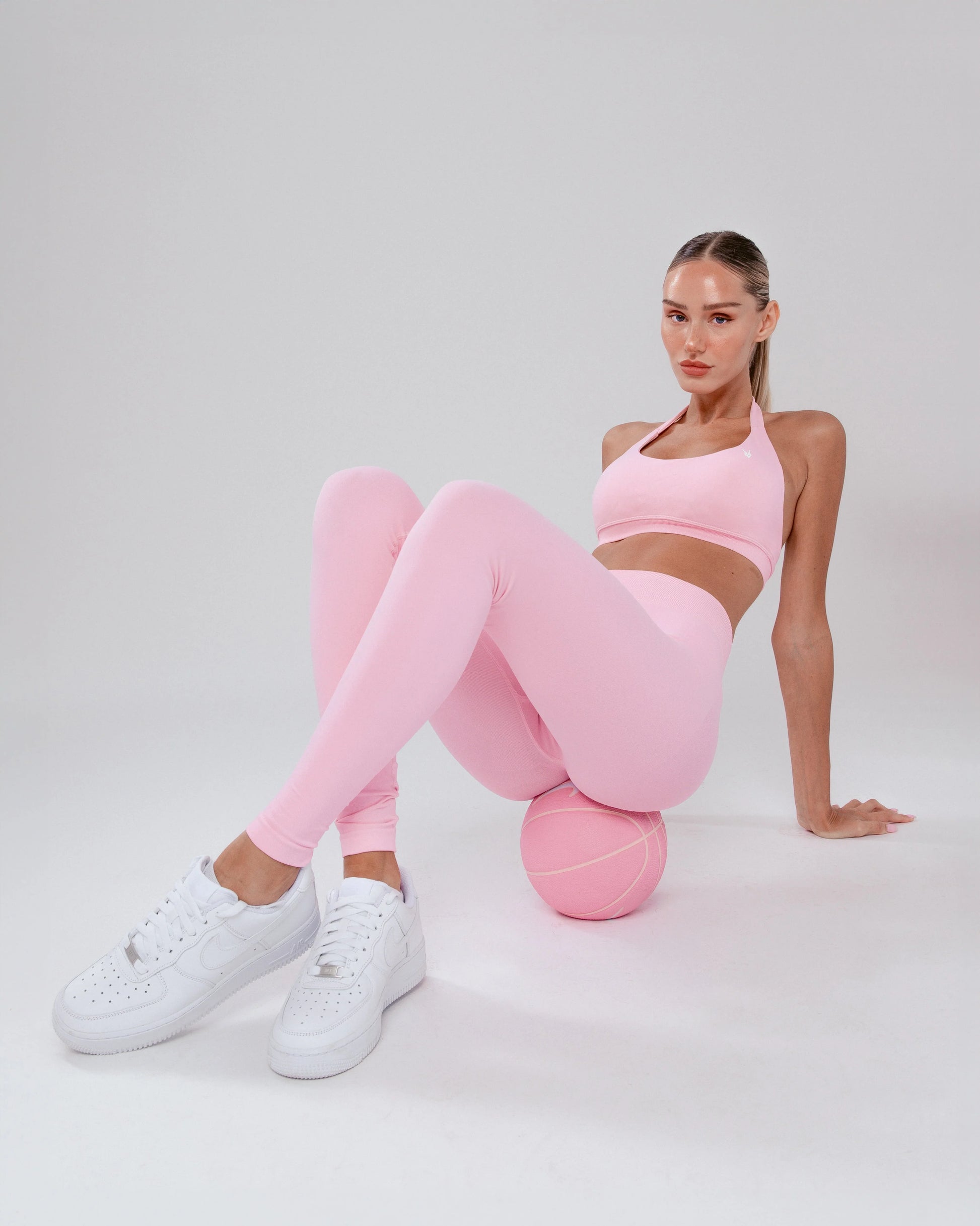 דוגמנית יושבת באווירה רגועה עם טייץ מחטב ורוד מסדרת AURA של Inner Dragon. בד חלק וגזרה מחמיאה באזור הישבן והמותן.