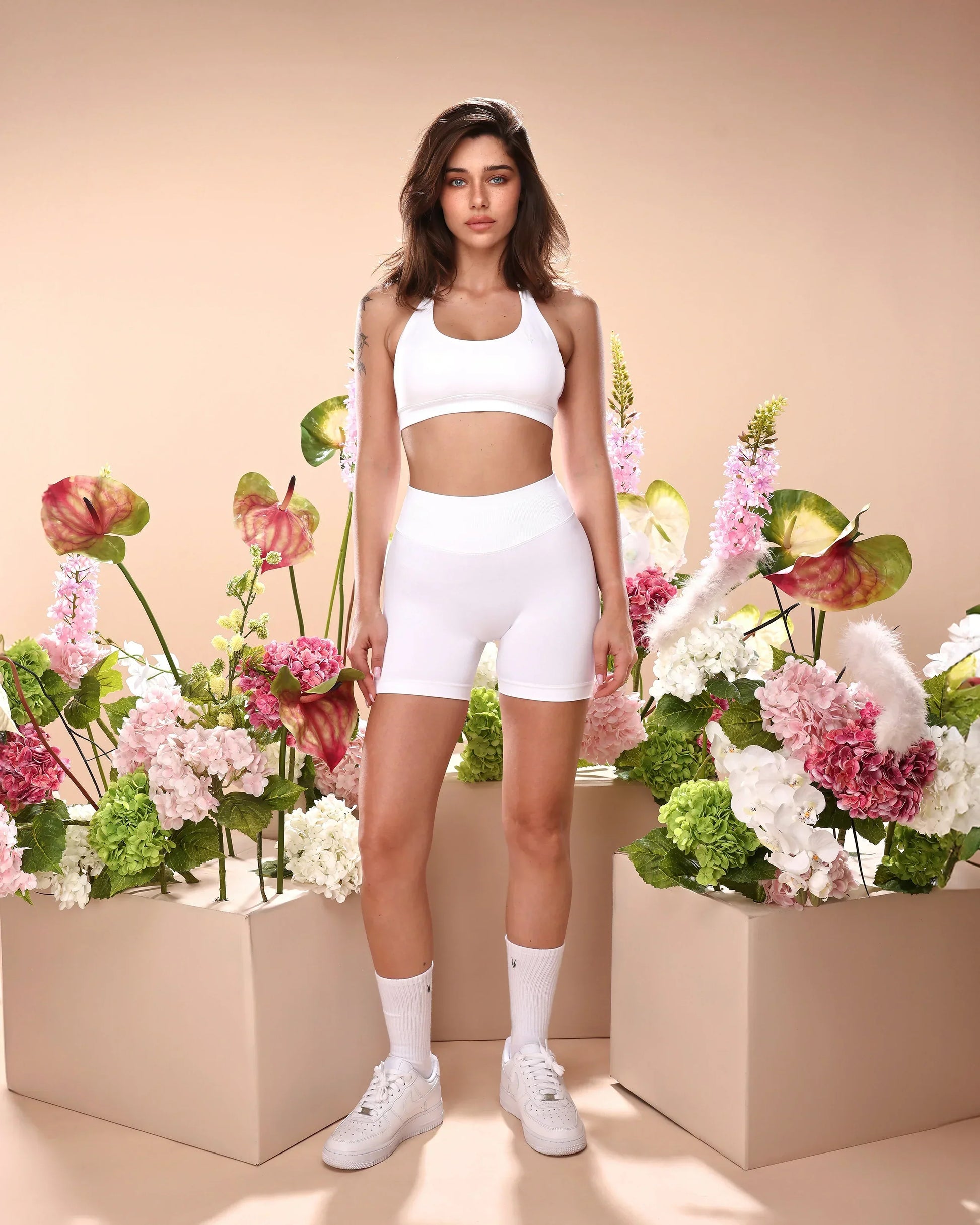 סט בגדי ספורט לנשים בצבע לבן – טופ AURA SNOW ללא תפרים ומכנסיים קצרים תואמים של Inner Dragon. דוגמנית עומדת בסטודיו, מראה את הסט במלואו. מושלם לכושר, יוגה, ריצה ופילאטיס – דגם מומלץ לנוחות, תמיכה ועיצוב מחמיא.