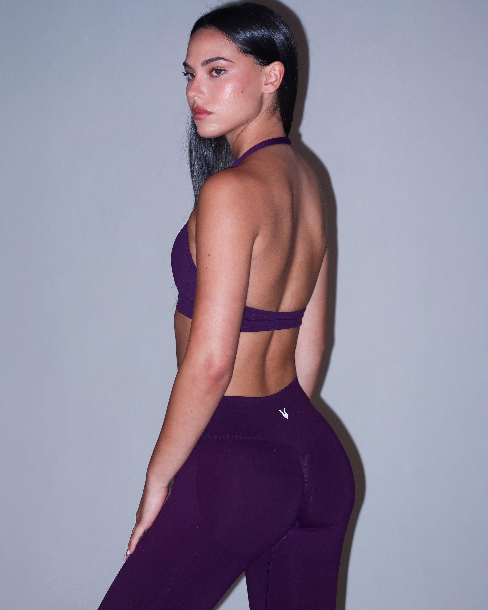 טייץ AURA VIOLET בגוון סגול עמוק – צילום אחורי המדגיש את הכיווץ הנסתר ואת מראה הישבן האסוף, בשילוב טופ הלטר תואם מבית Inner Dragon. טייץ מחטב בטכנולוגיית seamless ובד איכותי וגמיש לאימונים אינטנסיביים.