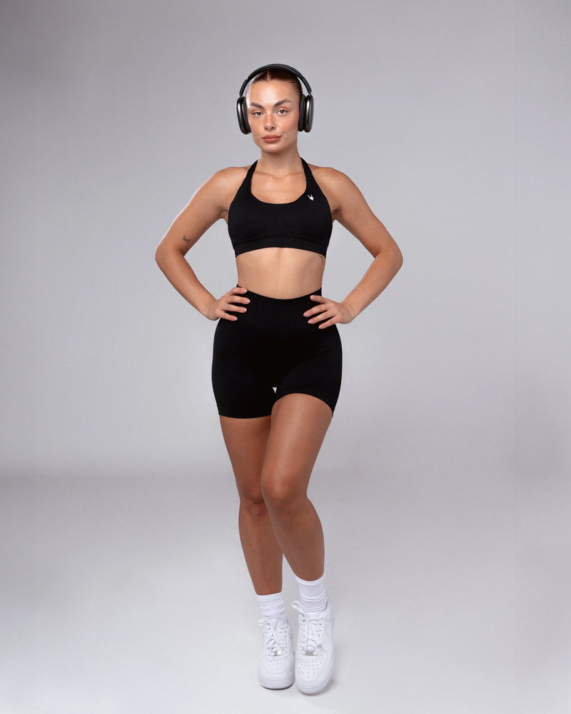 דוגמנית עם אוזניות לובשת שורט ספורט מחטב שחור HERA BLACK של אינר דרגון – תצוגה קדמית, טייץ קצר לאימון, עיצוב נשי, גזרה גבוהה, אופנת ספורט חדשנית לנשים
