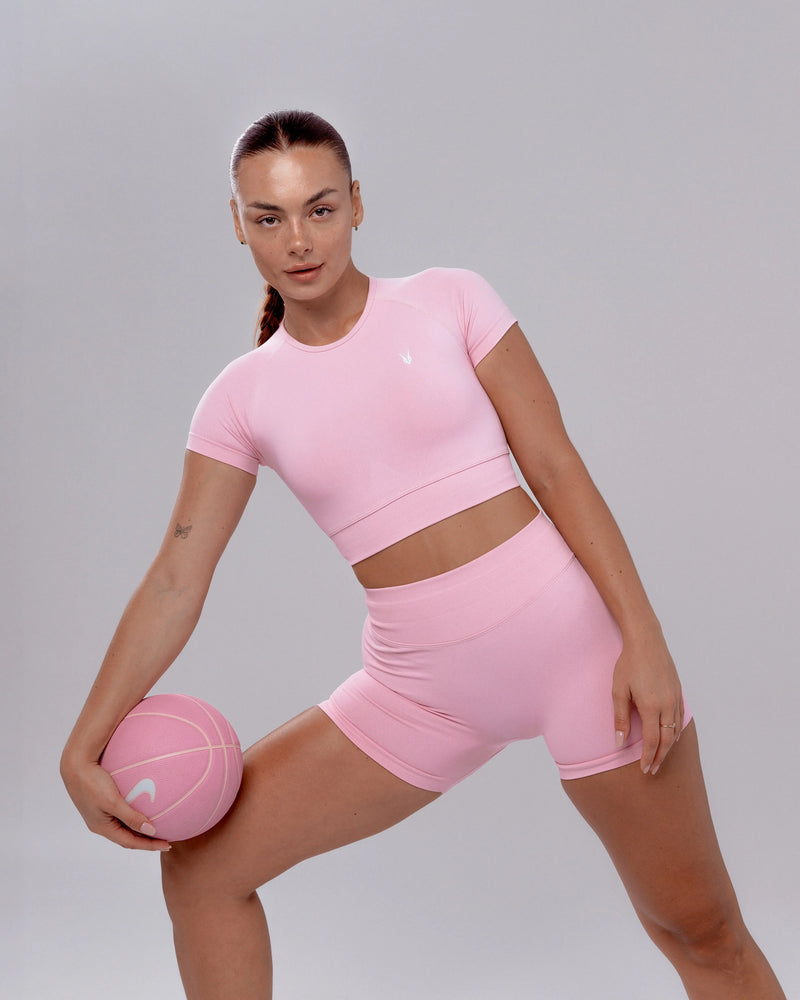 דוגמנית עם שורט ספורט ורוד מחטב וטופ תואם של Inner Dragon, בפוזת סקוואט עם כדור, בגד ספורט נשי בעיצוב מחמיא, טכנולוגיית seamless.