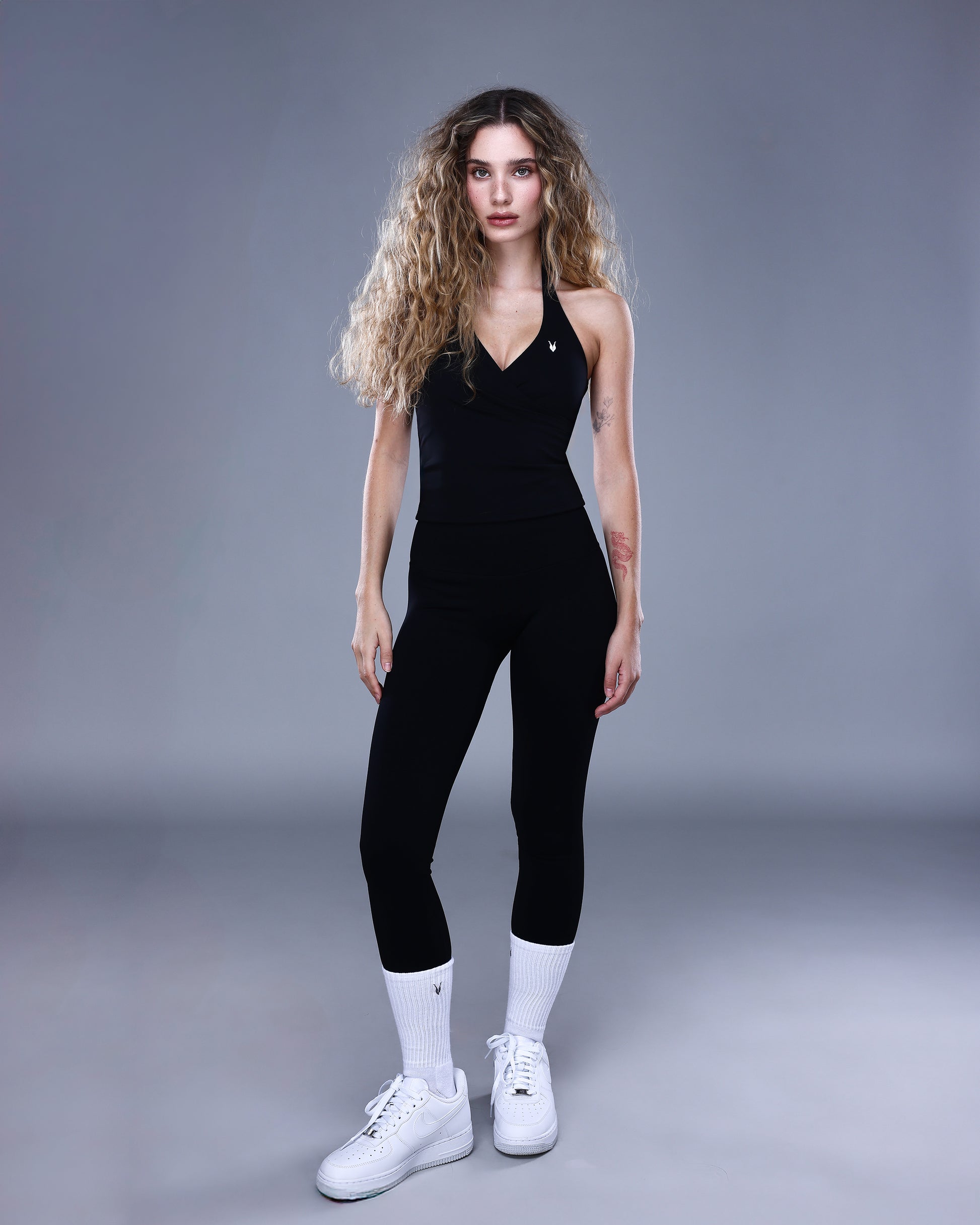 גופיית NAIA BLACK מבית Inner Dragon – גופיית ספורט שחורה עם גזרת מעטפת וגב פתוח, משולבת עם טייץ שחור לנשים. צילום גוף מלא באווירה אלגנטית, המשדר עוצמה, חיטוב וסטייל ספורטיבי־נשי.