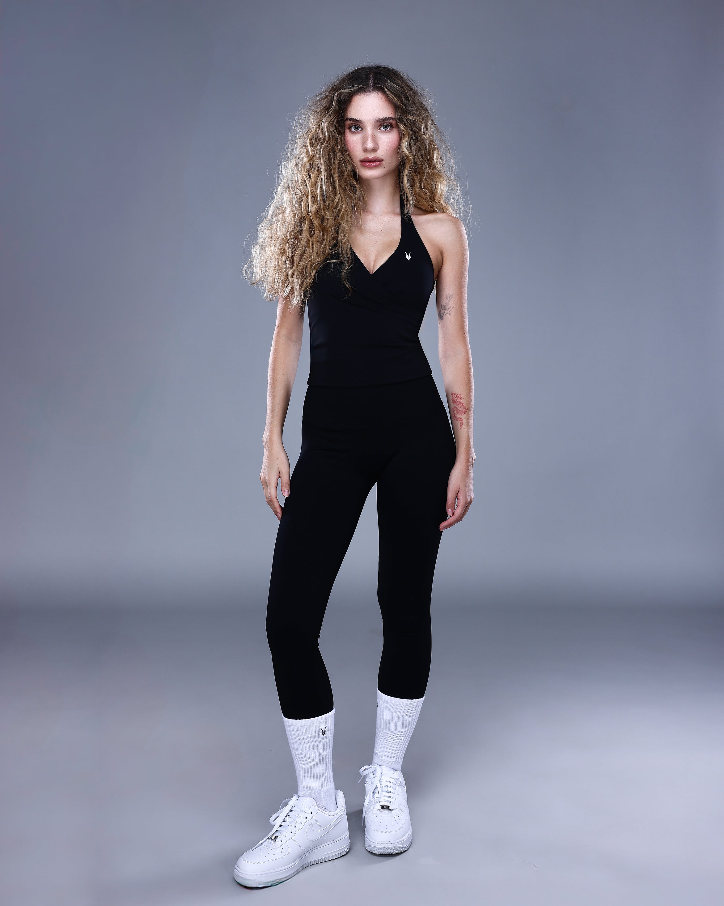 גופיית NAIA BLACK מבית Inner Dragon – גופיית ספורט שחורה עם גזרת מעטפת וגב פתוח, משולבת עם טייץ שחור לנשים. צילום גוף מלא באווירה אלגנטית, המשדר עוצמה, חיטוב וסטייל ספורטיבי־נשי.