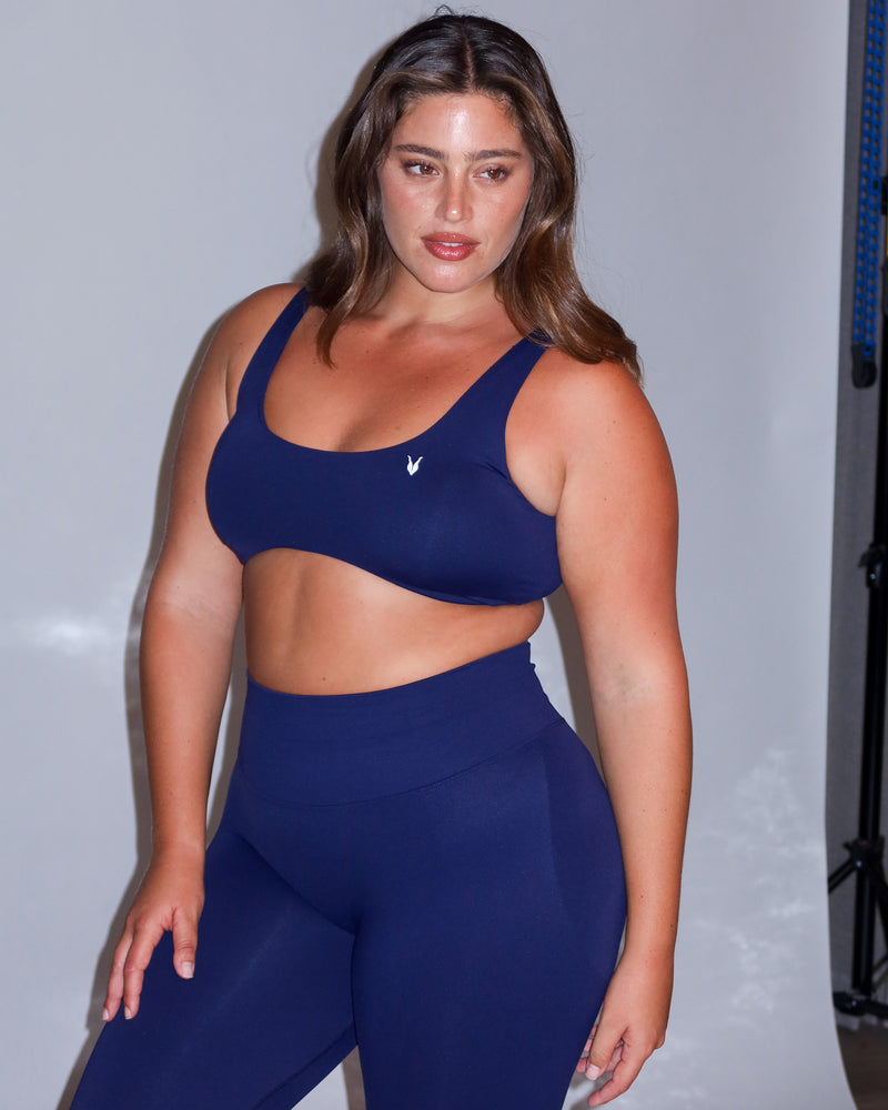 דוגמנית פלאס סייז לובשת סט ספורט לנשים בצבע כחול נייבי – טופ ונוס Deep Blue עם טייץ תואם. עיצוב מחטב ונוח לכל מבנה גוף.