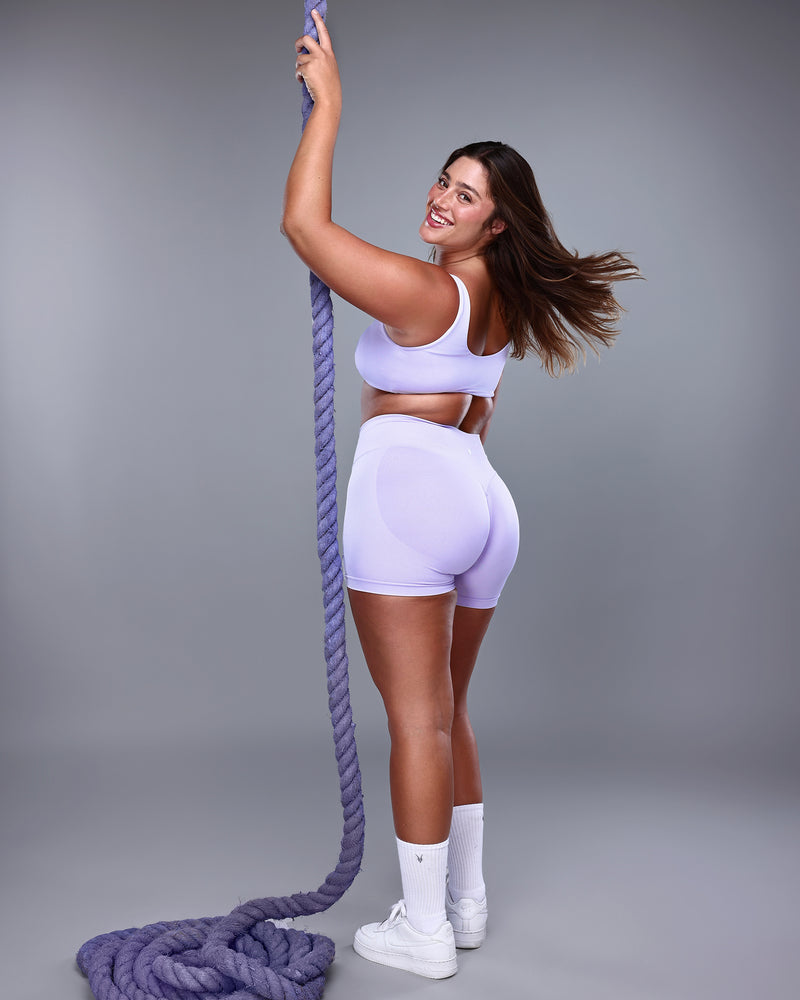 צילום אחורי של דוגמנית לובשת סט ספורט לונדר – טופ VENUS סגול בהיר ושורט תואם. הדגשה על הגב הפתוח והחיטוב באזור המותן והיריכייםן, בד seamless אלסטי, מותג Inner Dragon.