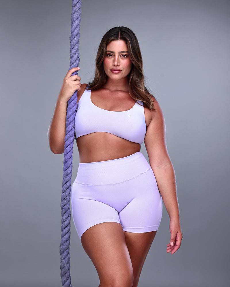 דוגמנית פלאס לובשת סט ספורט בצבע לונדר – טופ VENUS סגול בהיר ושורט תואם. צילום קדמי עם חבל אימון סגול ברקע, מראה מחטב ותומך, מותאם לאימוני כושר ויוגה. Inner Dragon.